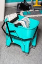 Turquoise bucket on wheels with an original rag wringing system on a gray background. Copy space