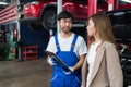 Professional vehicle maintenance man holding clipboard and talk with pretty lady customer. Repairman make a checklist and explain