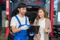 Professional vehicle maintenance man holding clipboard and talk with pretty lady customer. Repairman make a checklist and explain