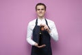 Professional waiter in uniform holds a bottle of red wine and smiles on a pink background, the sommelier recommends drinking wine Royalty Free Stock Photo