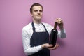 Professional waiter in uniform holds a bottle of red wine and smiles on a pink background, the sommelier recommends drinking wine Royalty Free Stock Photo