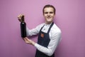 Professional waiter in uniform holds a bottle of red wine and smiles on a pink background, the sommelier recommends drinking wine Royalty Free Stock Photo