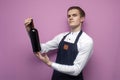 Professional waiter in uniform holds a bottle of red wine and smiles on a pink background, the sommelier recommends drinking wine Royalty Free Stock Photo