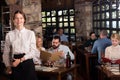 Professional waitress greeting customers at table in rustic restaurant