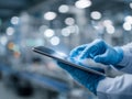 Professional wearing protective gloves using a digital tablet in a high-tech laboratory or manufacturing environment with blurred Royalty Free Stock Photo