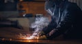 Professional welder in protective uniform with face mask, sparks fly apart, industrial welding close-up