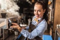 Professional, well-dressed female barista steams off coffee machine in a cafe