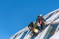 Professional window cleaners hanging on side of modern building against a blue sky