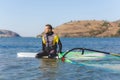 Professional windsurfer wearing wetsuit sitting on board and waiting for wind Royalty Free Stock Photo