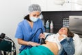 Professional woman cosmetician performing lifting procedure to mature woman on modern equipment in clinic