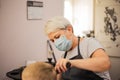 Professional woman hairdresser with face mask at work. Process of hair cutting at beauty salon. A boy gets a trendy haircut. Royalty Free Stock Photo