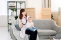 Professional woman pediatrician examining little baby girl by stethoscope. Doctor and baby sitting on gray sofa in Royalty Free Stock Photo