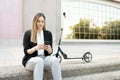 Professional woman resting outside a building and using her smartphone, sitting with a scooter Royalty Free Stock Photo