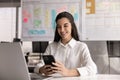Professional woman sits at desk using smartphone with contented smile Royalty Free Stock Photo