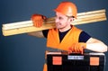 Professional woodworker concept. Man in helmet, hard hat holds toolbox and wooden beams, grey background. Carpenter
