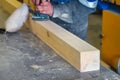 Professional woodworker grinds wooden bar on workbench in carpentry workshop with tool. Middle-aged worker in overalls