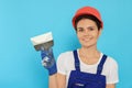 Professional worker in hard hat with putty knife on light blue background Royalty Free Stock Photo