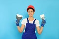 Professional worker in hard hat with putty knives on light blue background Royalty Free Stock Photo