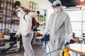 Professional workers in hazmat suits disinfecting indoor of cafe or restaurant, pandemic health risk, coronavirus