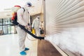 Professional workers in hazmat suits disinfecting indoor of mall, pandemic health risk, coronavirus