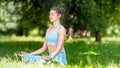 Professional yoga practitioner in blue tracksuit sits in relaxing lotus asana on green park meadow