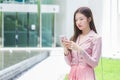 Professional young Asian business woman with long hair  smiling in front of the office while using a smartphone in her hand to Royalty Free Stock Photo