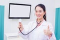 Professional young Asian woman doctor who wears medical uniform and stethoscope standing with is showing hand as thump up Royalty Free Stock Photo