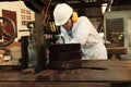 Professional young Asian worker in white uniform and safety equipment cutting a piece of wood on vertical band saw machine in carp Royalty Free Stock Photo