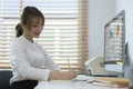 Professional young businesswoman reading statistics graphs on screen of computer and making notes on notebook Royalty Free Stock Photo