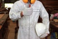 Professional young carpenter in white uniform showing thump up with pencil tools in carpentry workshop.