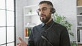 Professional young man with beard working indoors in a modern office, wearing a headset and speaking Royalty Free Stock Photo