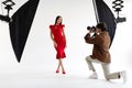 Professional young man photographer capturing portraits of elegant lady in red dress, woman posing on white background Royalty Free Stock Photo