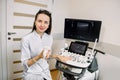 Professional young woman doctor sonographer sitting nearby modern ultrasound scanner machine and smiling Royalty Free Stock Photo