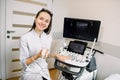 Professional young woman doctor sonographer sitting nearby modern ultrasound scanner machine and smiling Royalty Free Stock Photo