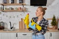 Professional young woman wearing rubber protective yellow gloves holding bottle cleaners in the kitchen.