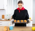 Proffesional woman in chef uniform holding sheet pan with just baked cupcakes