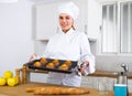 Proffesional woman cook in white uniform holding sheet pan with just baked cupcakes