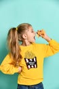 Profile of a beautiful happy girl in a yellow hoodie tasting french fries on a green background