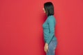 Profile of beautiful middle aged woman with black hair in blue blouse and jeans . indoor studio shot isolated on red Royalty Free Stock Photo