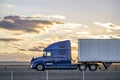 Profile of big rig blue semi truck tractor with dry van semi trailer driving on the flat highway road along the fields at twilight Royalty Free Stock Photo