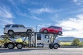 Profile of big rig classic semi truck car hauler with loaded hydraulic semi trailer running on the highway road Royalty Free Stock Photo