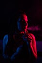 Profile of caucasian girl with dreadlocks smokes a vape in red blue light.