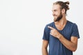 Profile of cheerful handsome man with fashionable hairstyle and beard smiling brightfully and pointing at free space for