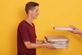 Profile of cheerful pleasant young boy holding cardboard boxes with pizza, unknown hands putting one more box, smiling sincere,