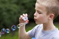 Profile of cute handsome small blond child boy with funny serious expression blowing colorful transparent soap bubbles outdoors o Royalty Free Stock Photo