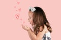 Profile of little girl in white dress and headband blowing on her hands and sending kiss and hearts on pink background Royalty Free Stock Photo