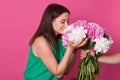 Profile of cute smiling girl with closed eyes smelling flowers with colorful petals, touching them with both hands, being in high Royalty Free Stock Photo