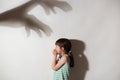 Profile of female kid frightened by the shadows of hands of demons, scared little girl suffering from sciophobia and phantoms,