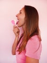 Profile of funny girl lick a heart shape lollipop at pink wall at background. Valentines day