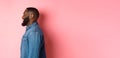 Profile of handsome bearded Black guy standing over pink background, smiling and looking left at copy space